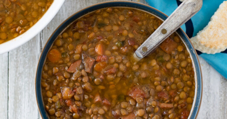 a bowl filled with Crock Pot Ham and Lentils soup with a plate of biscuits in the background